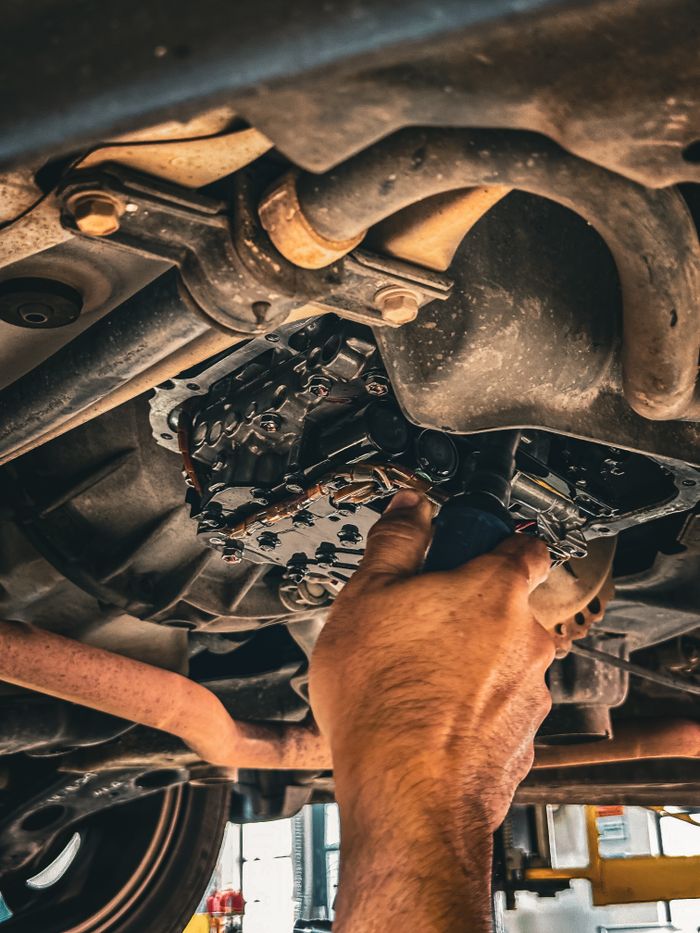 About Mechanic working on car undercarriage in a garage setting.