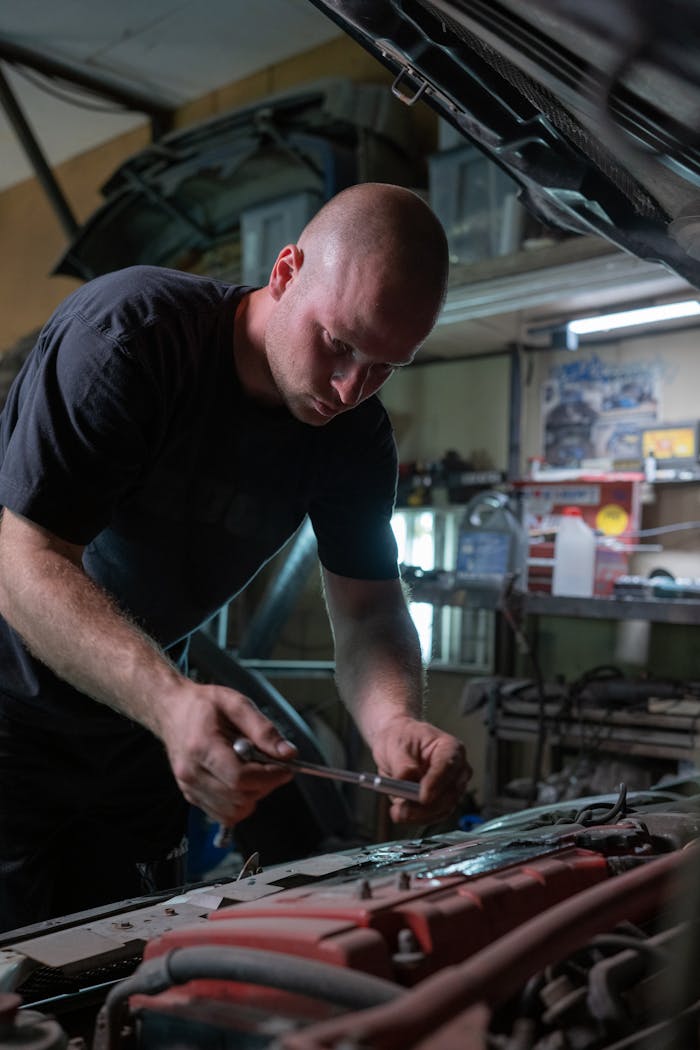 About A mechanic is diligently working inside a garage, fixing a car engine under the hood.